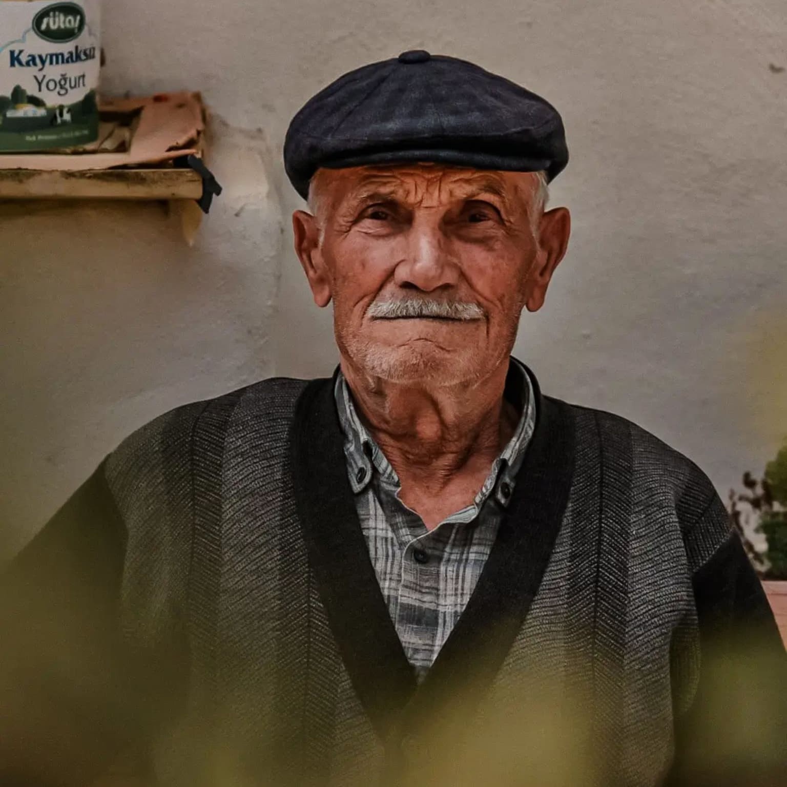 An elderly woman with short white hair resting her hand on her head, her face turned into warm sunlight