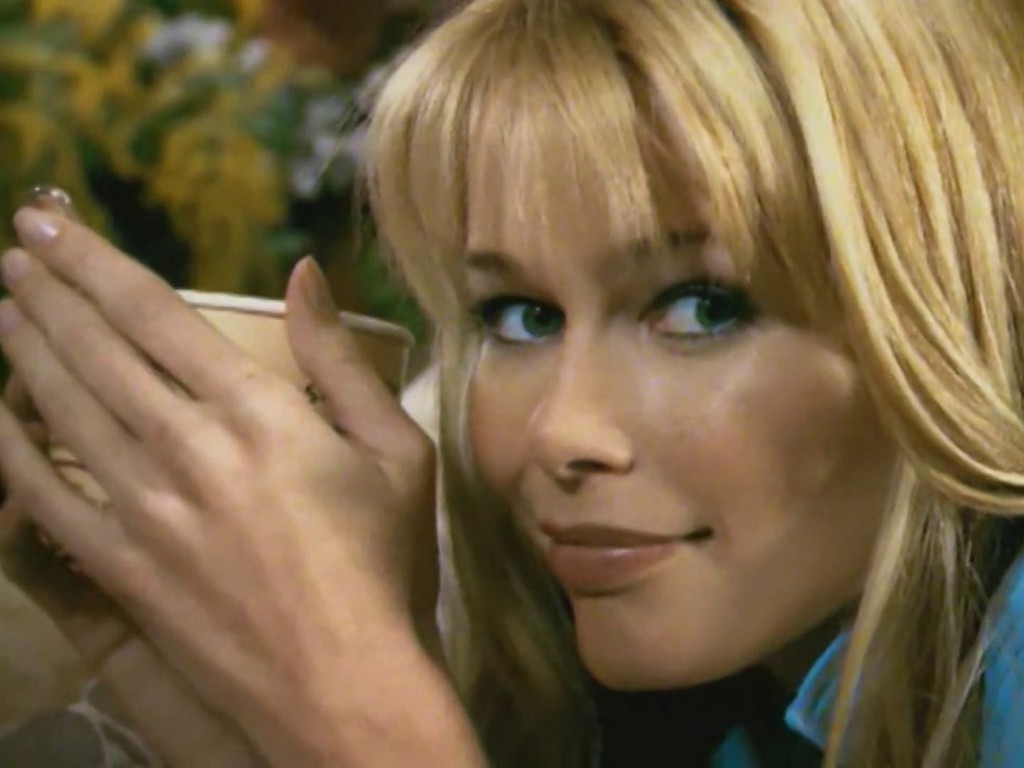 Claudia Schiffer holding a Cape Byron cup in a sunlit room with yellow flowers