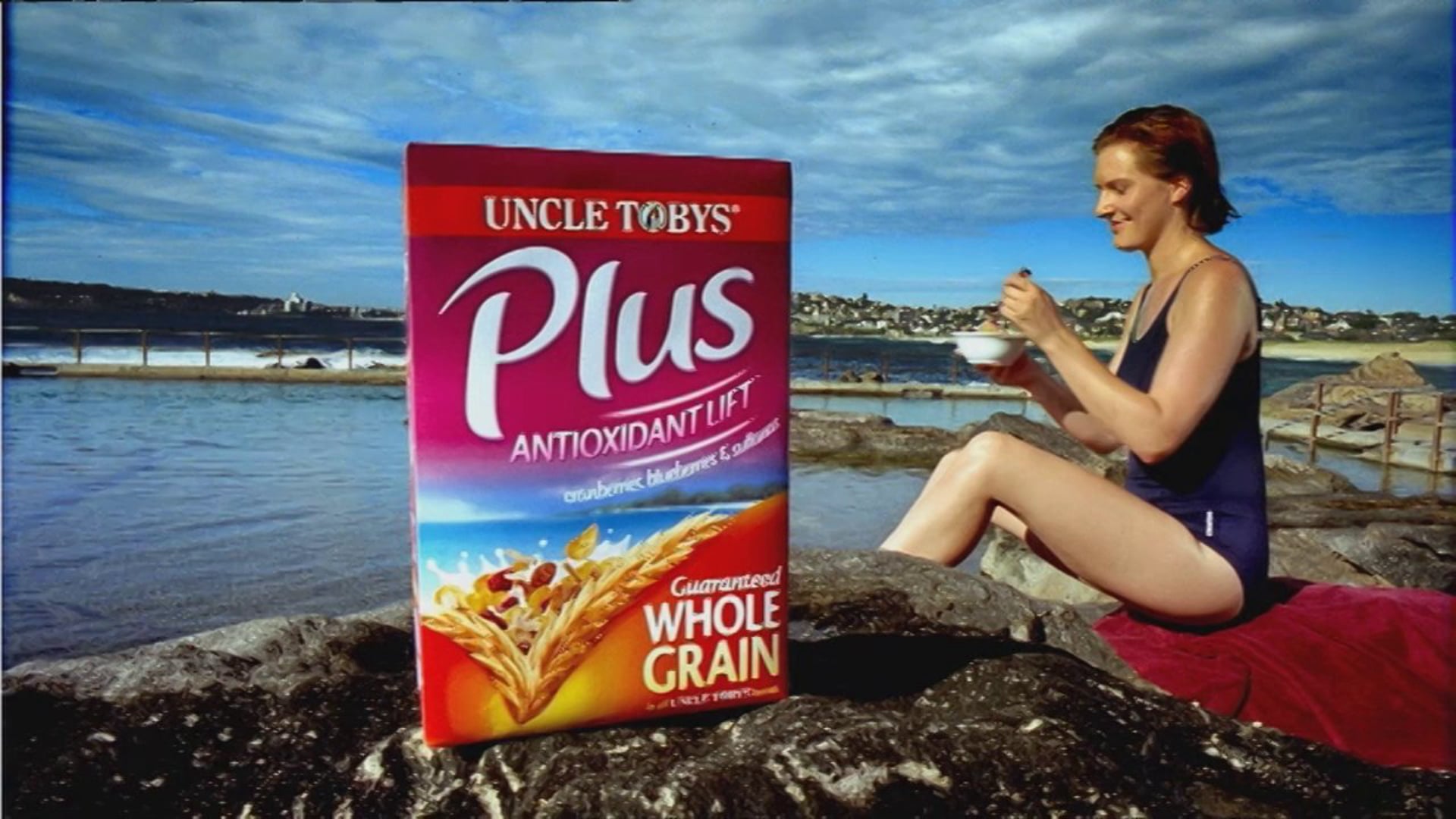 Woman enjoying Uncle Toby's Plus cereal by a coastal rock pool